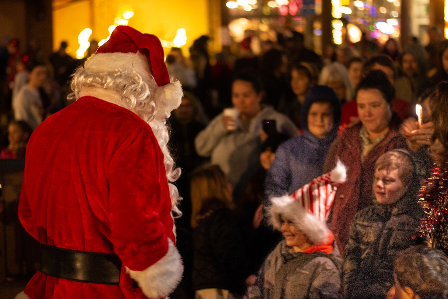 Santa Claus faces a crowd of children and families during the Coos Bay Tree Lighting Ceremony, as kids smile and gather close in the warm glow of holiday lights.