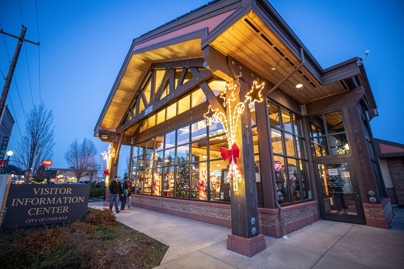 The Coos Bay Visitor Information Center is decorated with holiday lights and a Christmas tree inside, welcoming shoppers exploring local gift shops, museum stores, and businesses featuring Oregon-made goods across Coos Bay, North Bend, and Charleston.