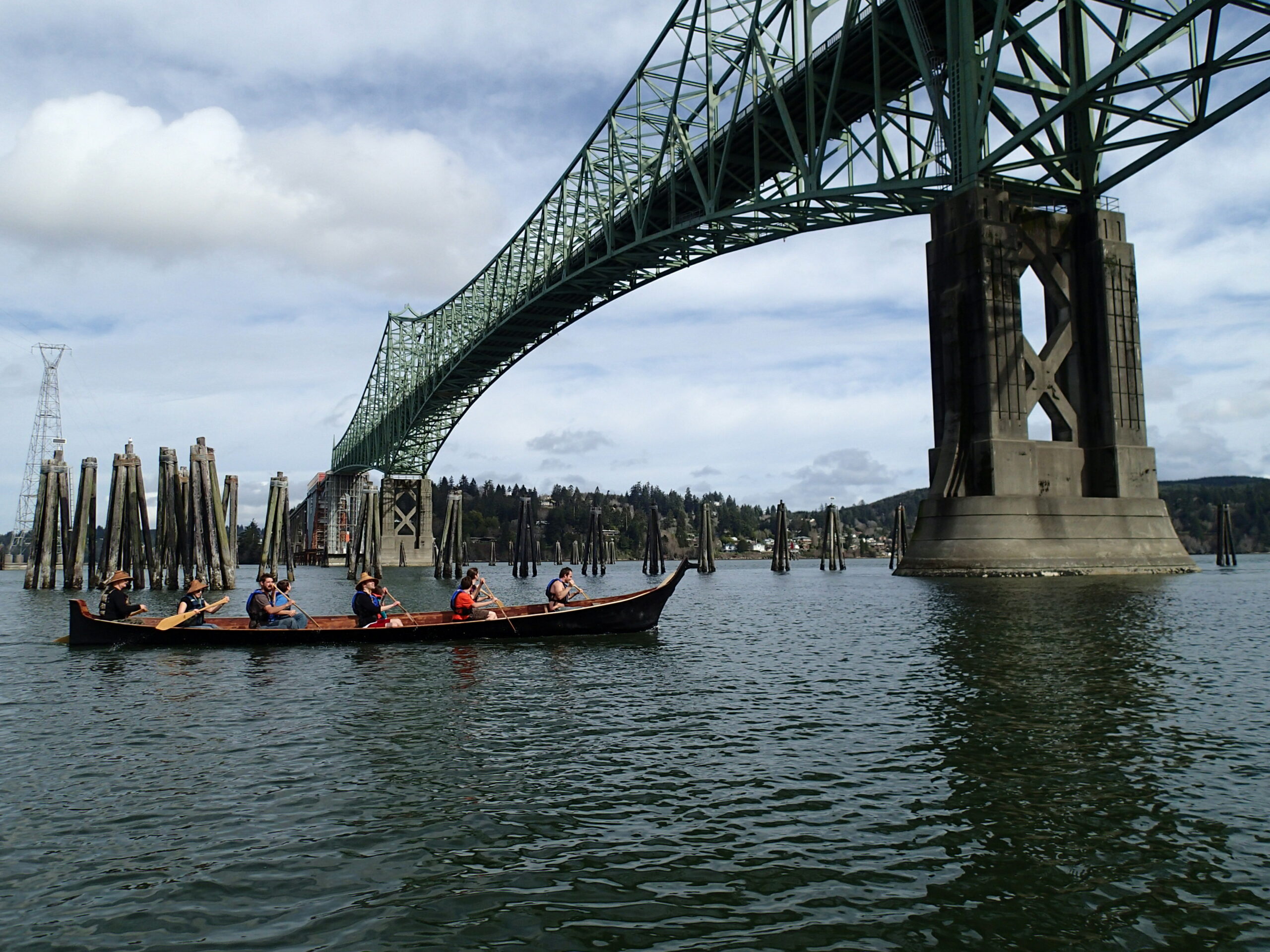 A canoe is paddled by tribal members under the North Bend Bridge.