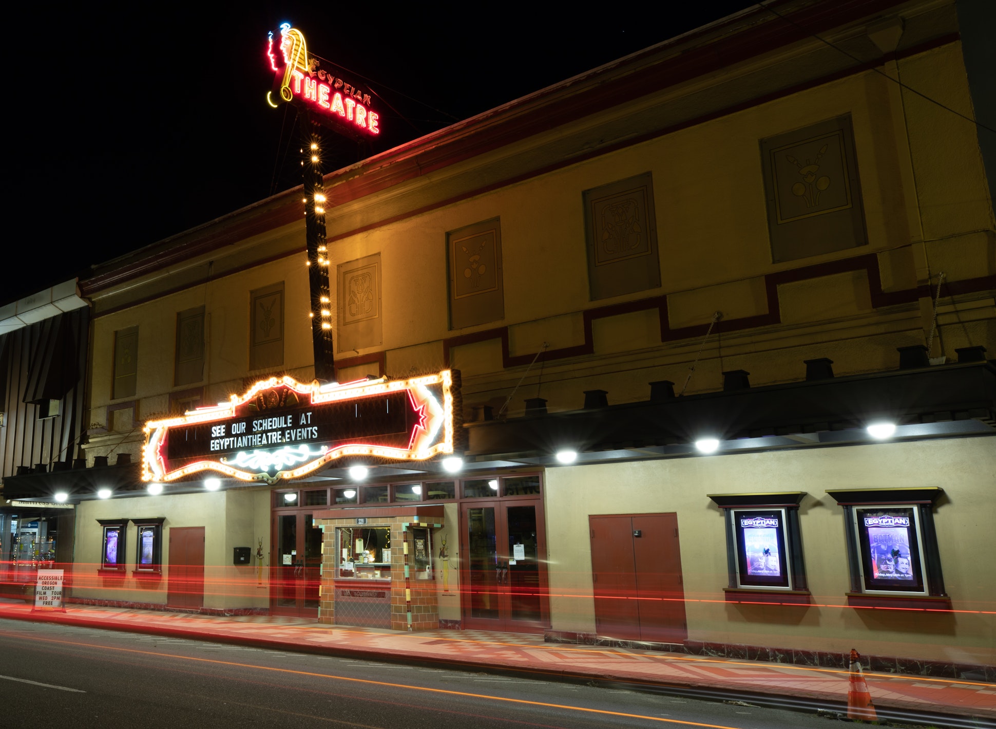 Nighttime street view of the historic Egyptian Theatre in downtown Coos Bay, Oregon, with its illuminated marquee and neon sign.
