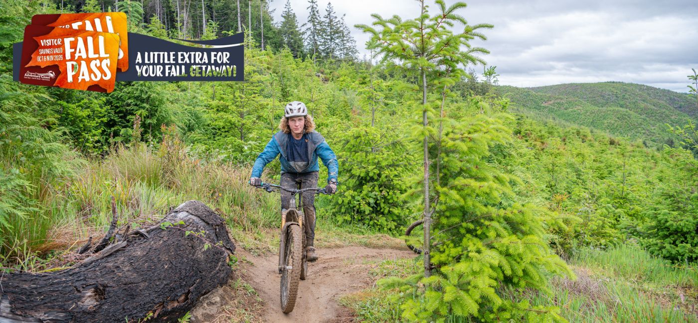 Mountain biker riding a forest trail past evergreen trees, with Fall Pass promotional badge