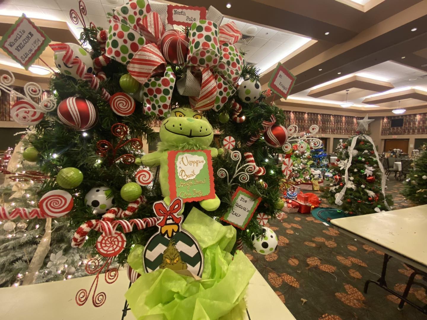 A brightly decorated Christmas tree with a Grinch theme stands among dozens of festive trees at the Festival of Trees Holiday Showcase and Benefit Auction at Ko-Kwel Casino Resort in Coos Bay, where local businesses display creative designs for the annual Rotary Club fundraiser.
