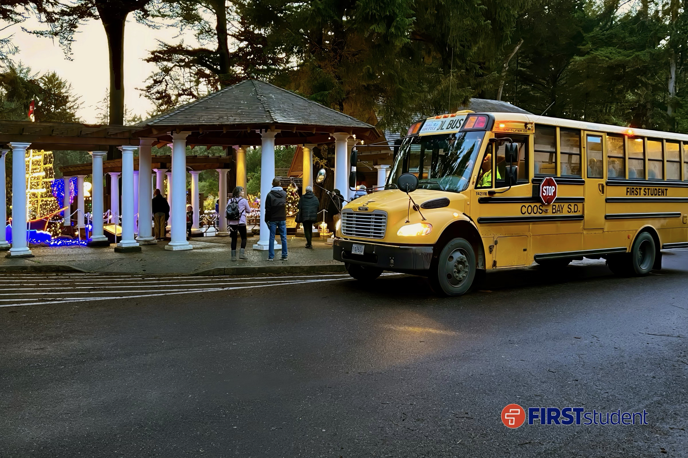 A bus drops off visitors near the illuminated entrance pavilion at Shore Acres State Park during the Annual Holiday Lights event, where complimentary shuttles from the Charleston Marina help guests arrive for the festive displays, warm drinks, and family activities.
