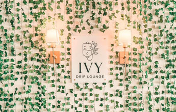 IVY Drip Lounge Sign on wall with ivy and sconces.