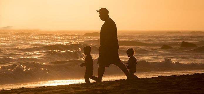 Kids and father silhouette at beach at sunset.
