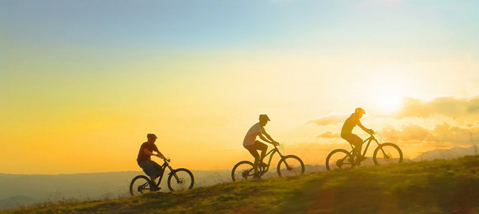 Three bikers on crest of hill in silhouette at Sunset
