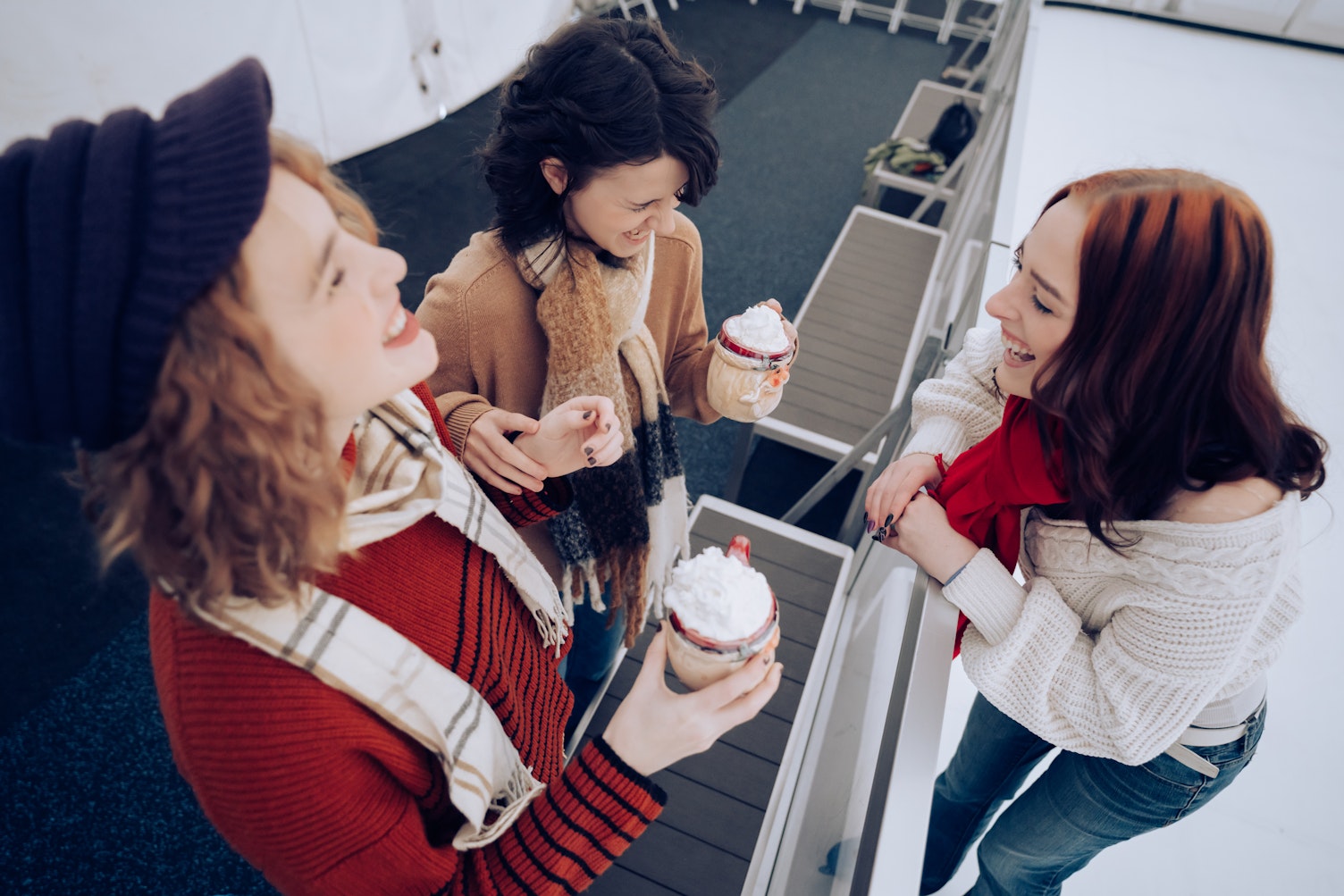 Three friends laugh together while holding hot drinks beside the ice rink in Downtown North Bend, where visitors can enjoy the only ice skating rink on the Oregon Coast now through January 31, 2026.