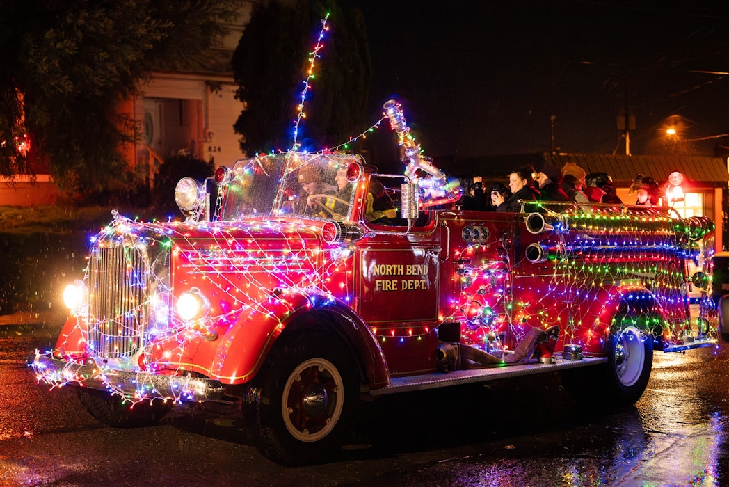 A vintage North Bend Fire Department truck covered in colorful holiday lights drives through Downtown North Bend during the Lighted Truck Parade, part of the city’s Christmas on Main celebration.